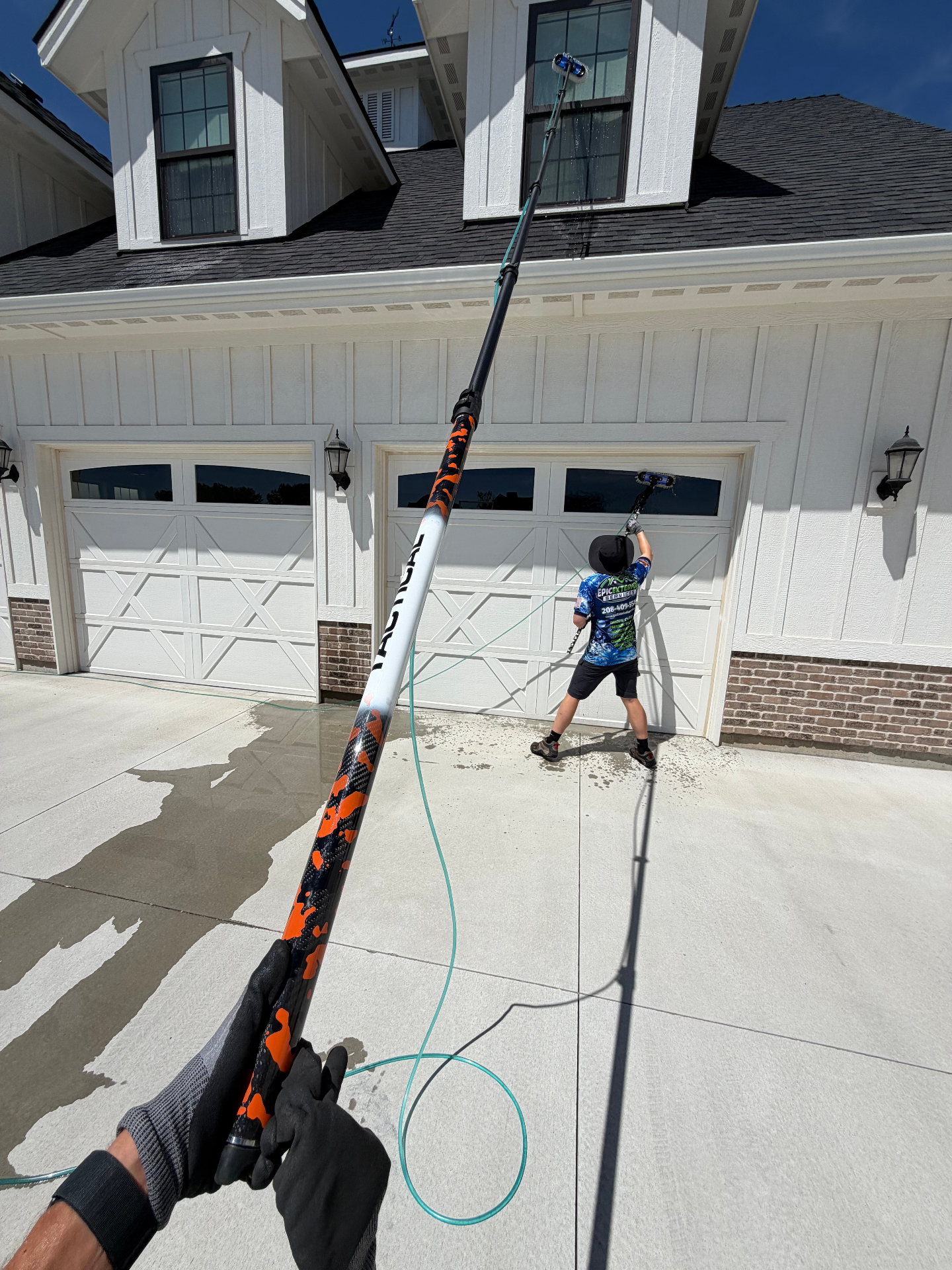 Exterior second-story window cleaning on a white home using a long water-fed pole